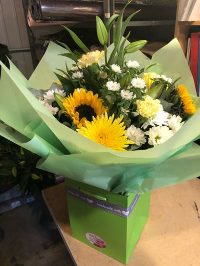 Golden Glow - Brighten someone's day with the `Golden Glow` arrangement, featuring a stunning sunflower mix with seasonal blooms. Complemented by lush green foliage, this arrangement brings a touch of nature's radiant beauty into any space.